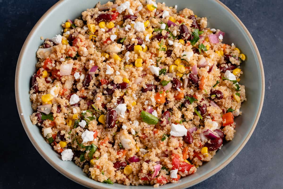 horizontal photo of vegan quinoa salad in large blue bowl with wooden spoon