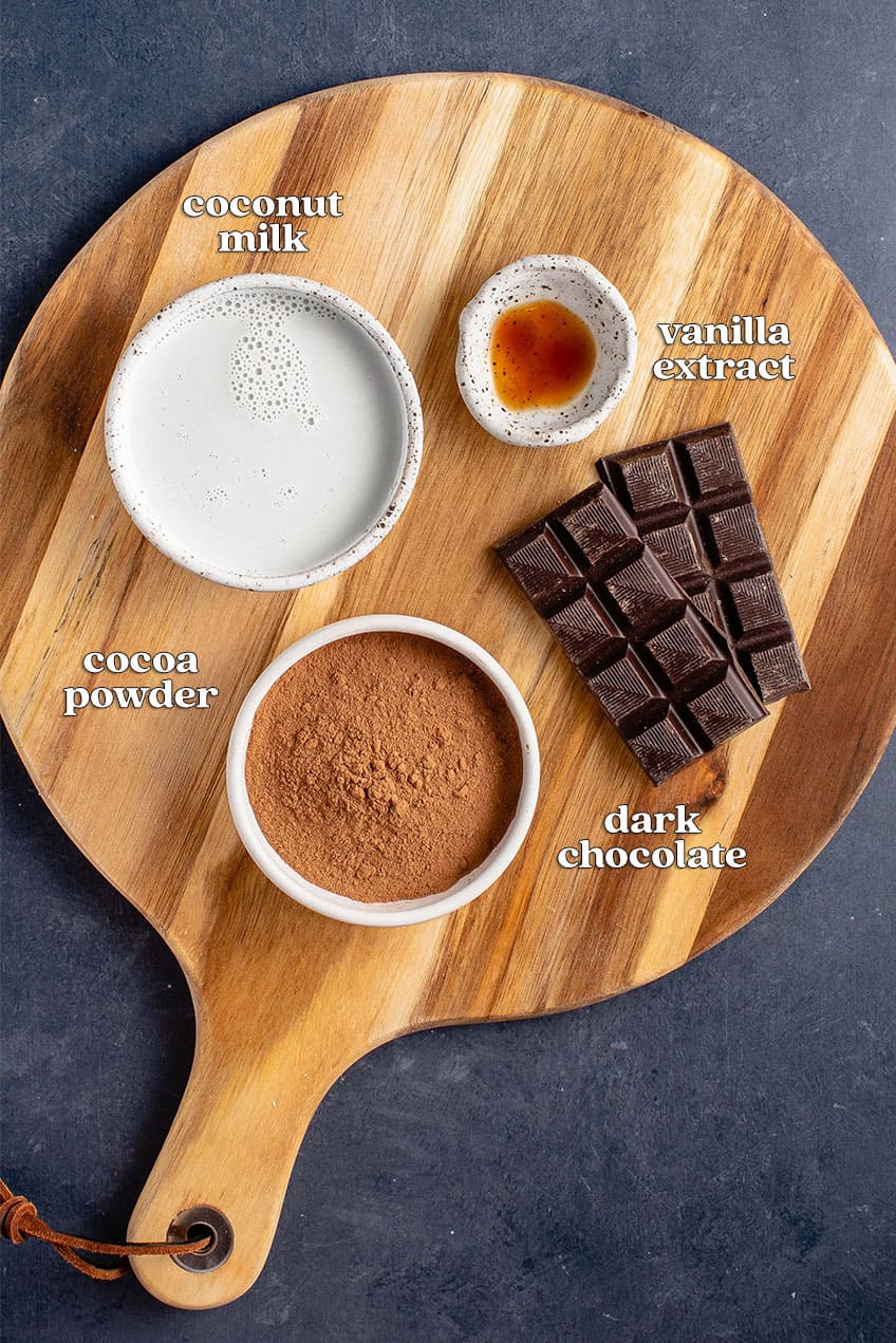 coconut milk, vanilla extract, cocoa powder and dark chocolate on wooden board