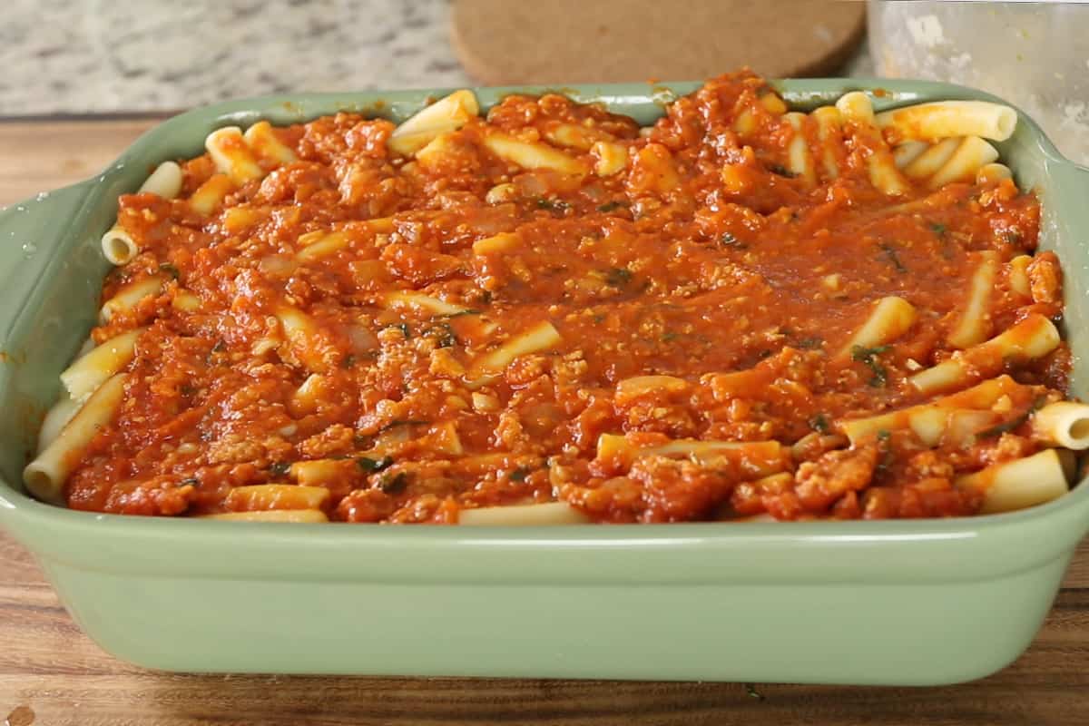 layering noodles sauce and cheese in green baking dish for baked ziti