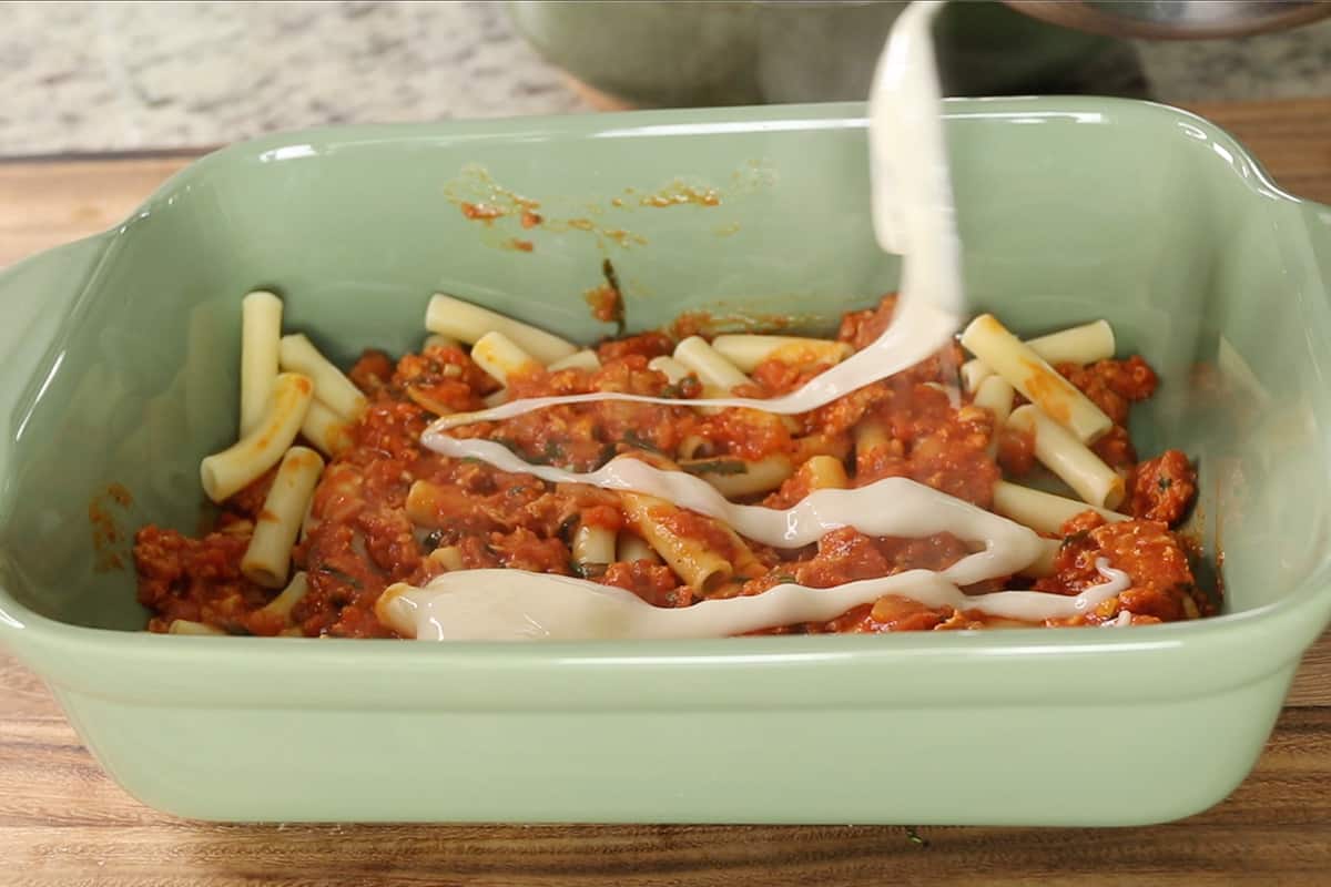 laying noodles sauce and cheese in green baking dish for baked ziti