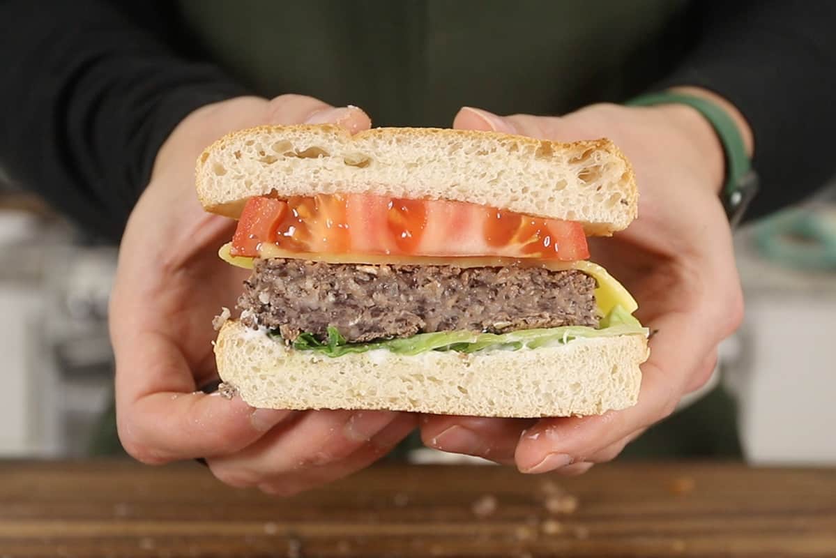hands holding a halved black bean burgerwith lettuce, tomato, cheese and mayonnaise