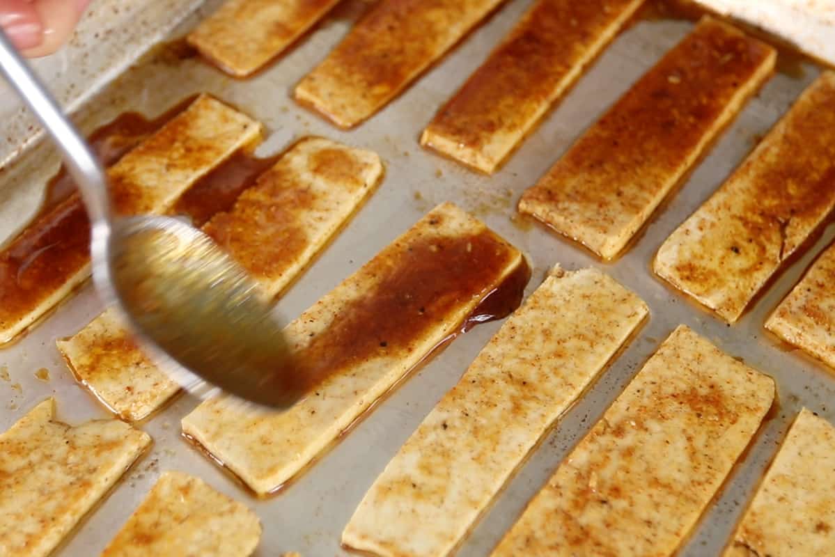 pouring sauce on tofu pieces on baking sheet