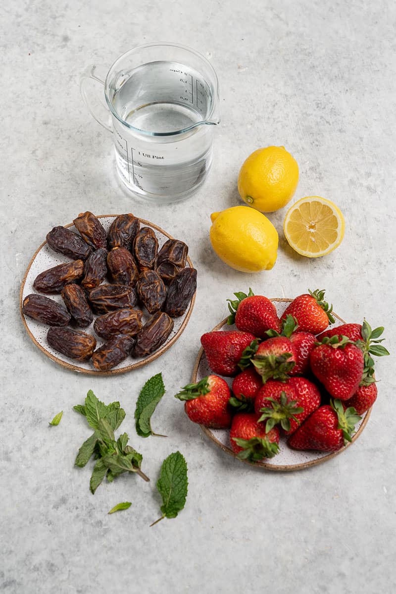 dates, strawberries, lemons, and a cup of water on a white table