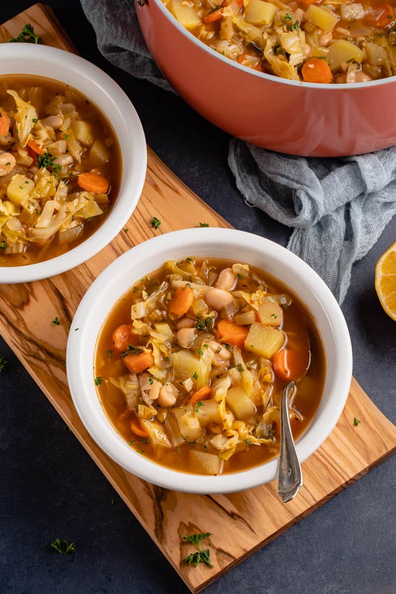 white bowls with vegan cabbage soup and metal spoon