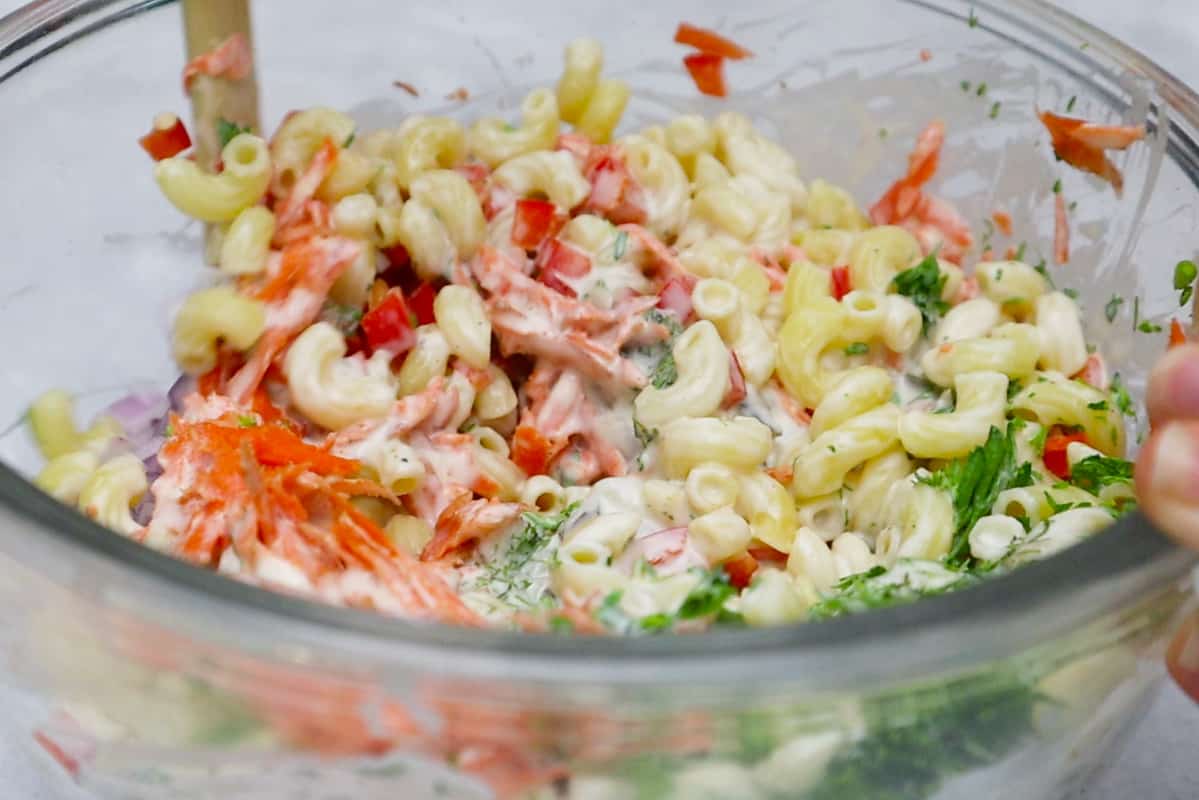 mixing vegan macaroni salad in glass bowl