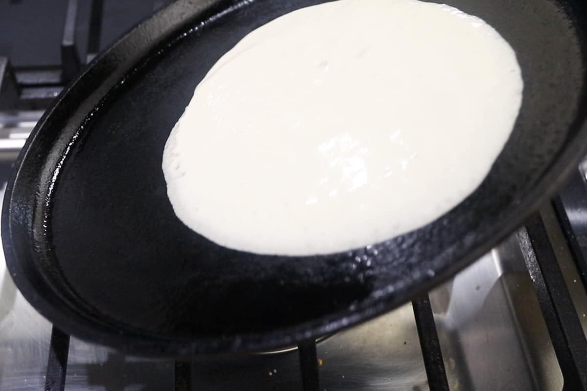 spreading crepe batter onto cast iron griddle pan