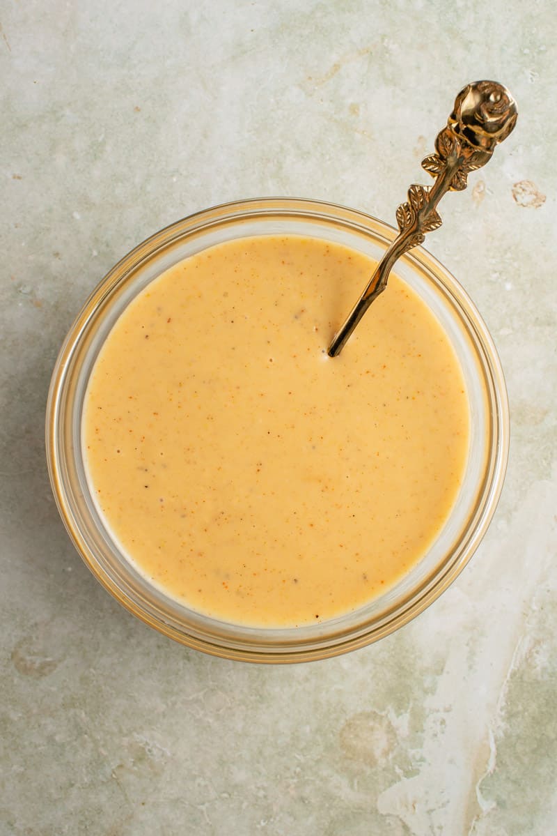 spoon with vegan honey mustard dressing in glass bowl