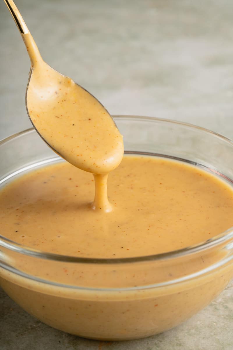 spoon with vegan honey mustard dressing in glass bowl
