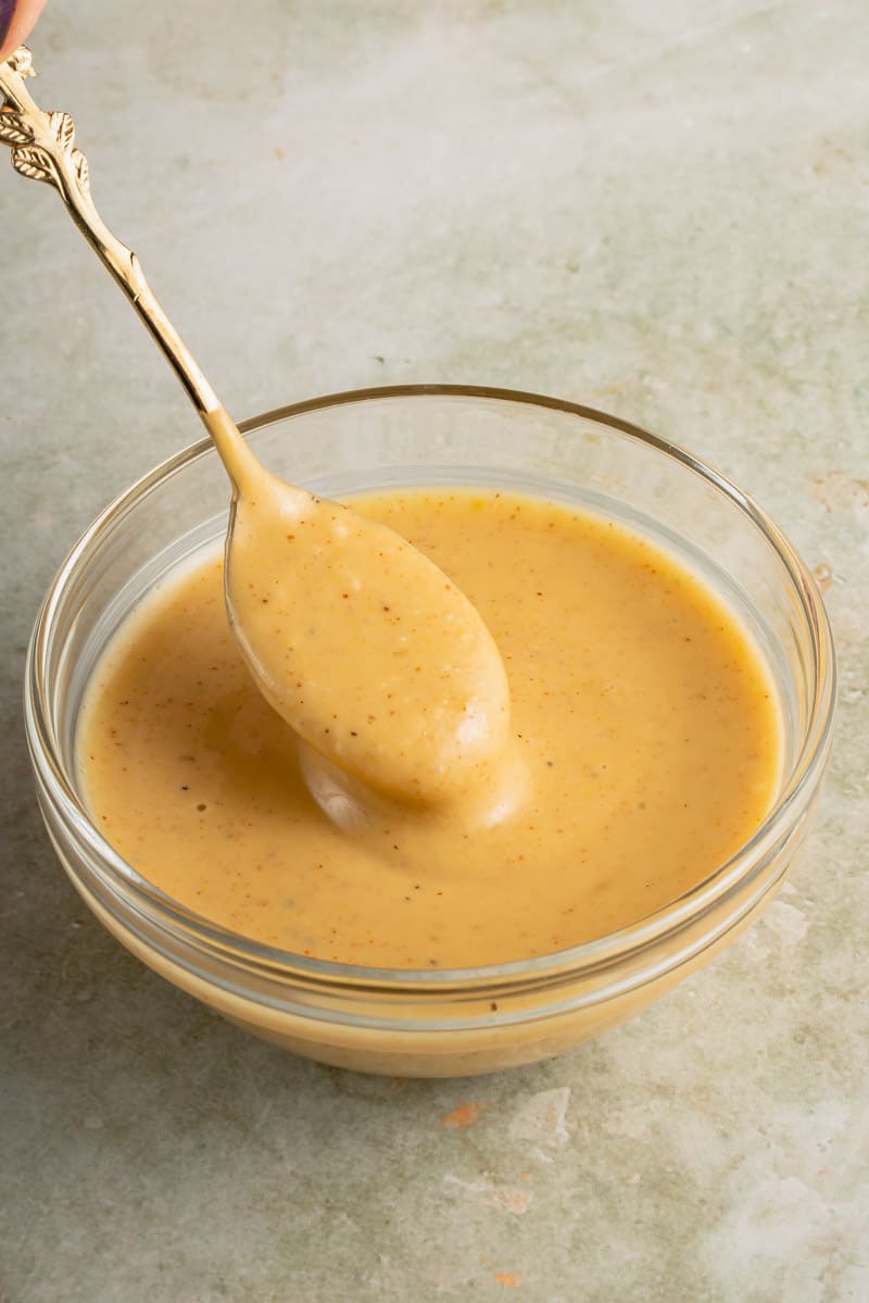 spoon with vegan honey mustard dressing in glass bowl