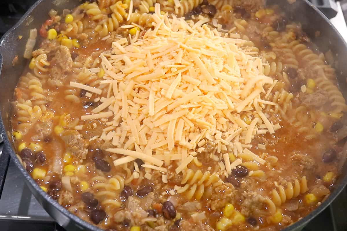 adding vegan cheddar cheese to taco pasta in black pot