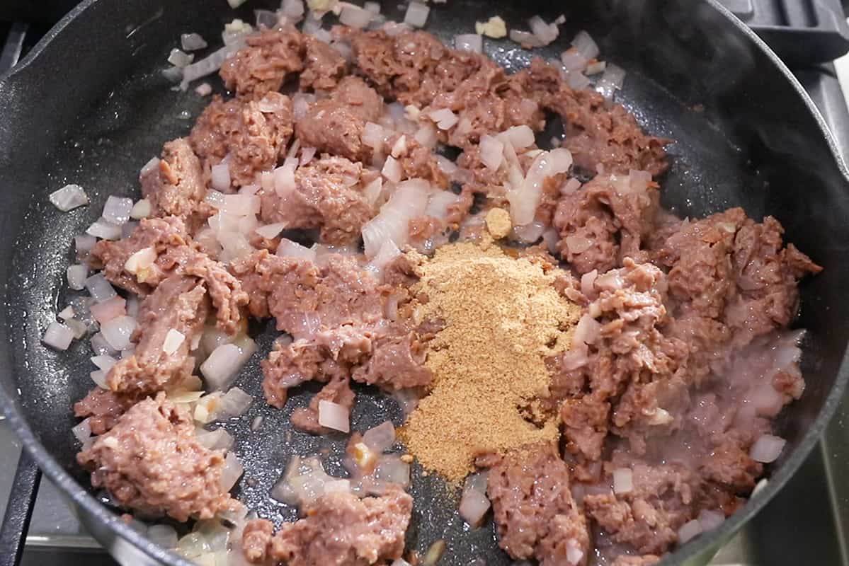 adding spices to onions and beyond meat in black pan