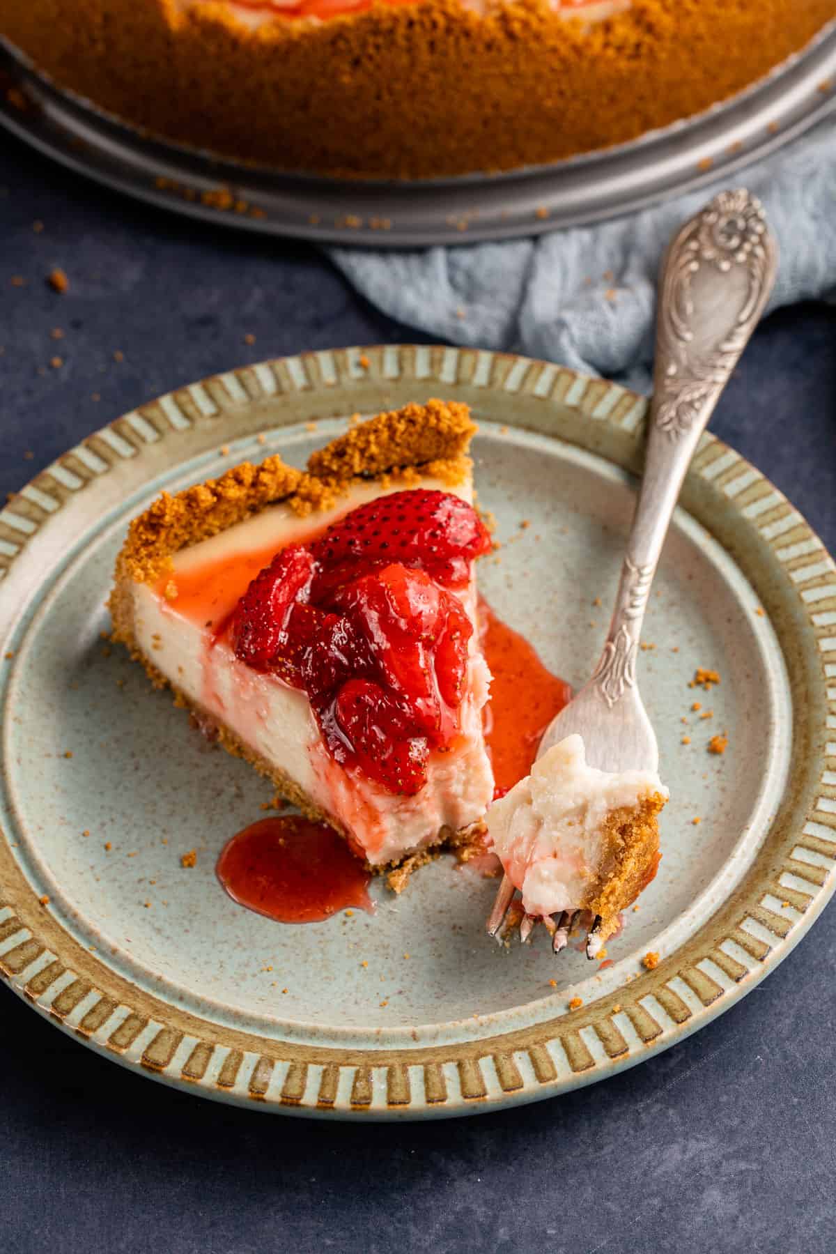slice of vegan cheesecake with strawberry sauce on light blue plate