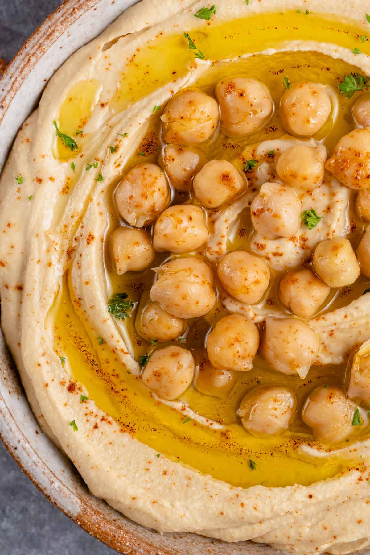 close up photo of creamy hummus topped with chickpeas, olive oil and parsley