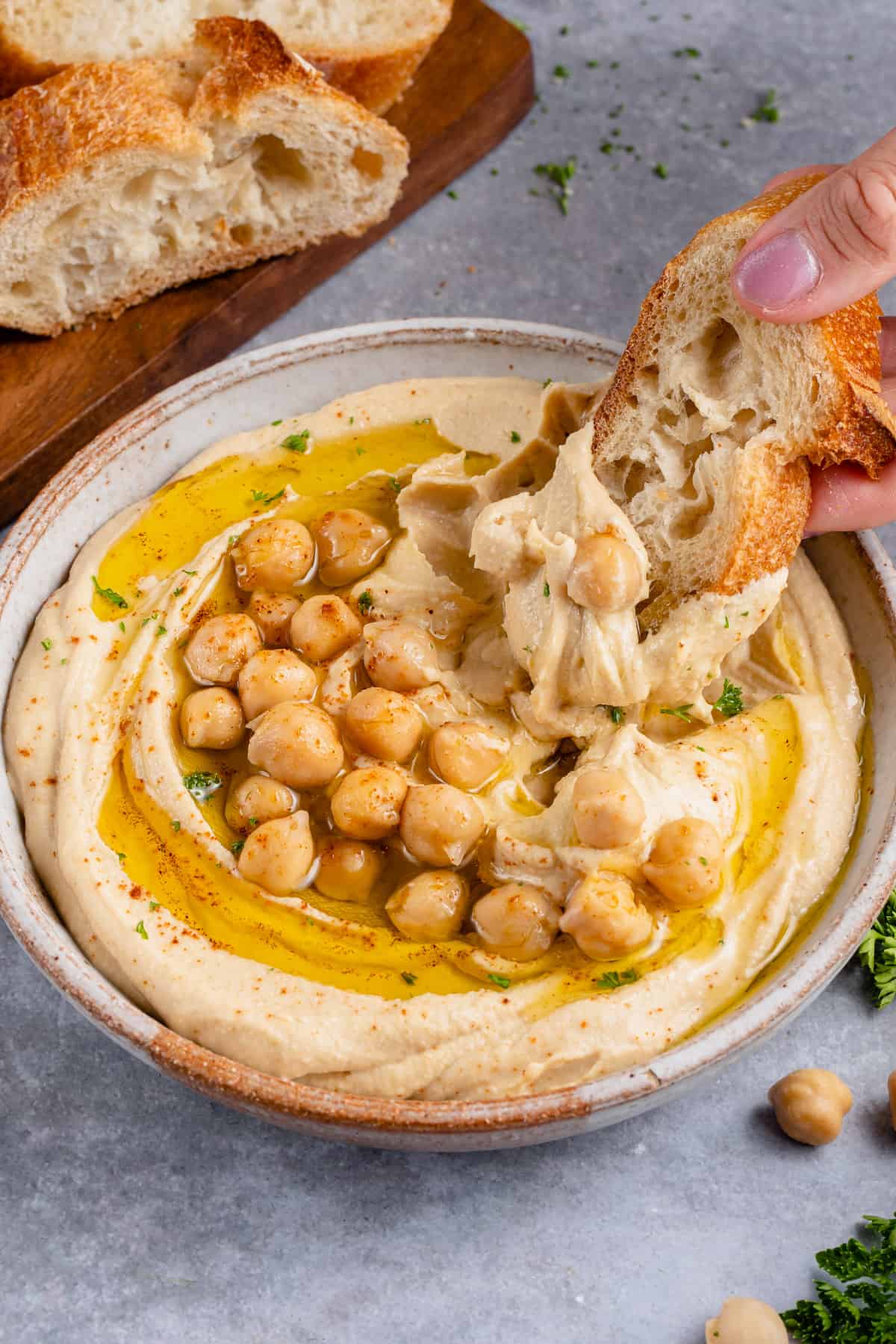 dipping toasted bread into creamy hummus on a gray board