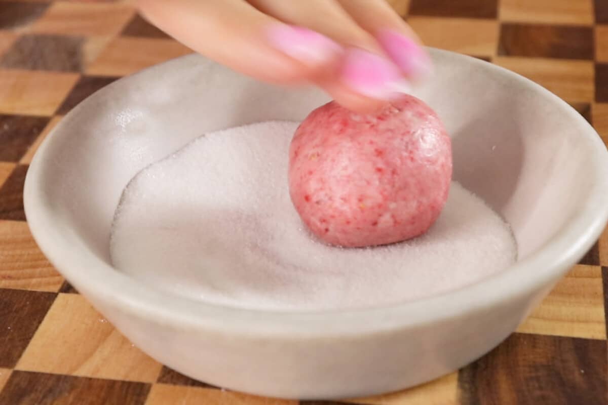 rolling ball of strawberry cookie dough in sugar