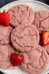 strawberry sugar cookies stacked on a speckled white plate with fresh strawberry slices