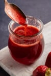scooping strawberry syrup with metal spoon in glass jar