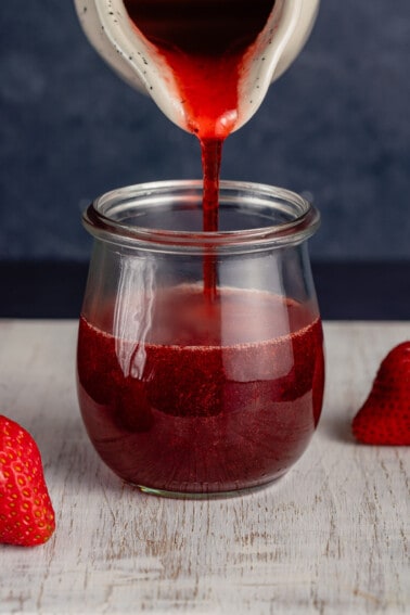 pouring strawberry syrup into a glass jar