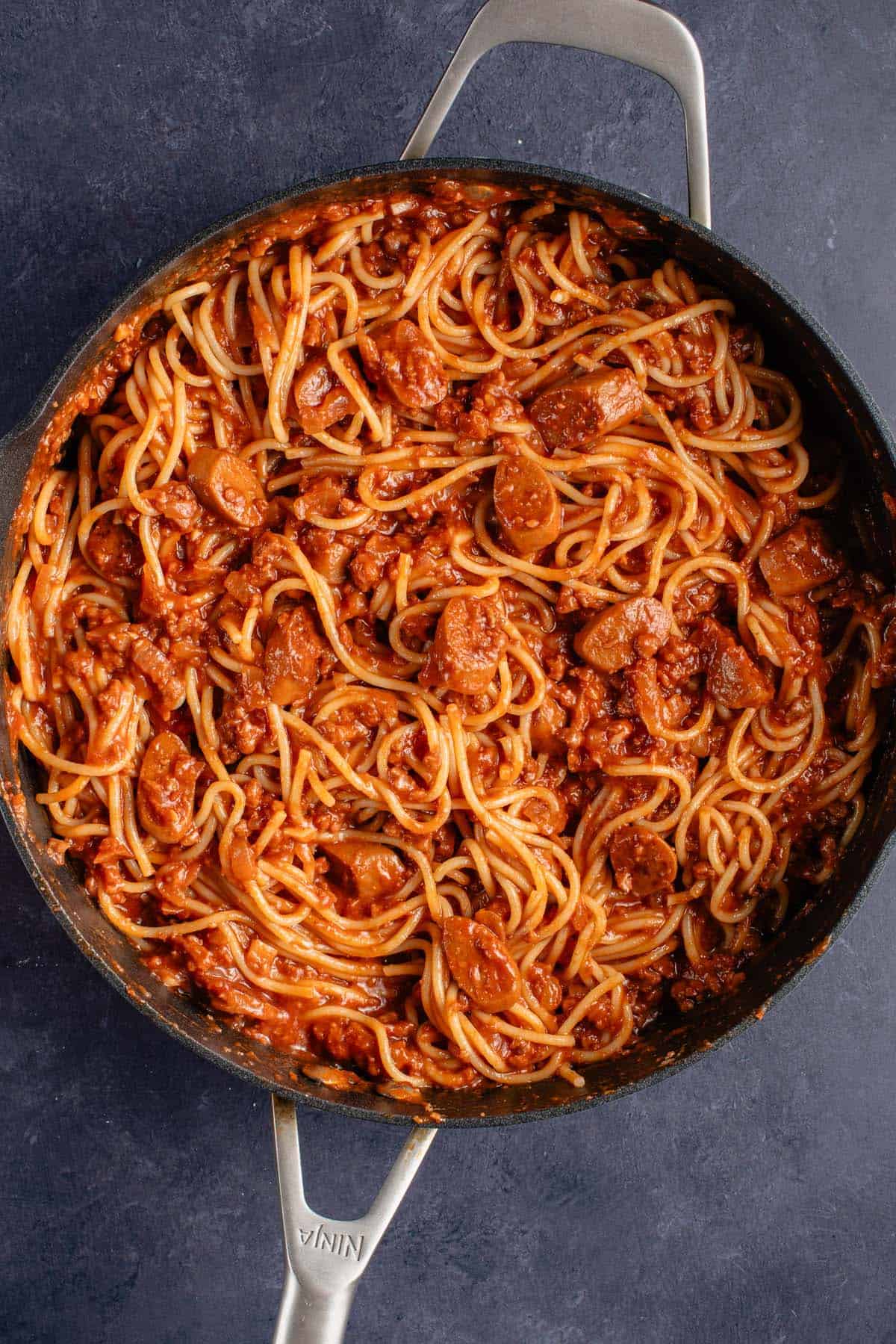 overhead photo of filipino spaghetti with hot dogs in black pan