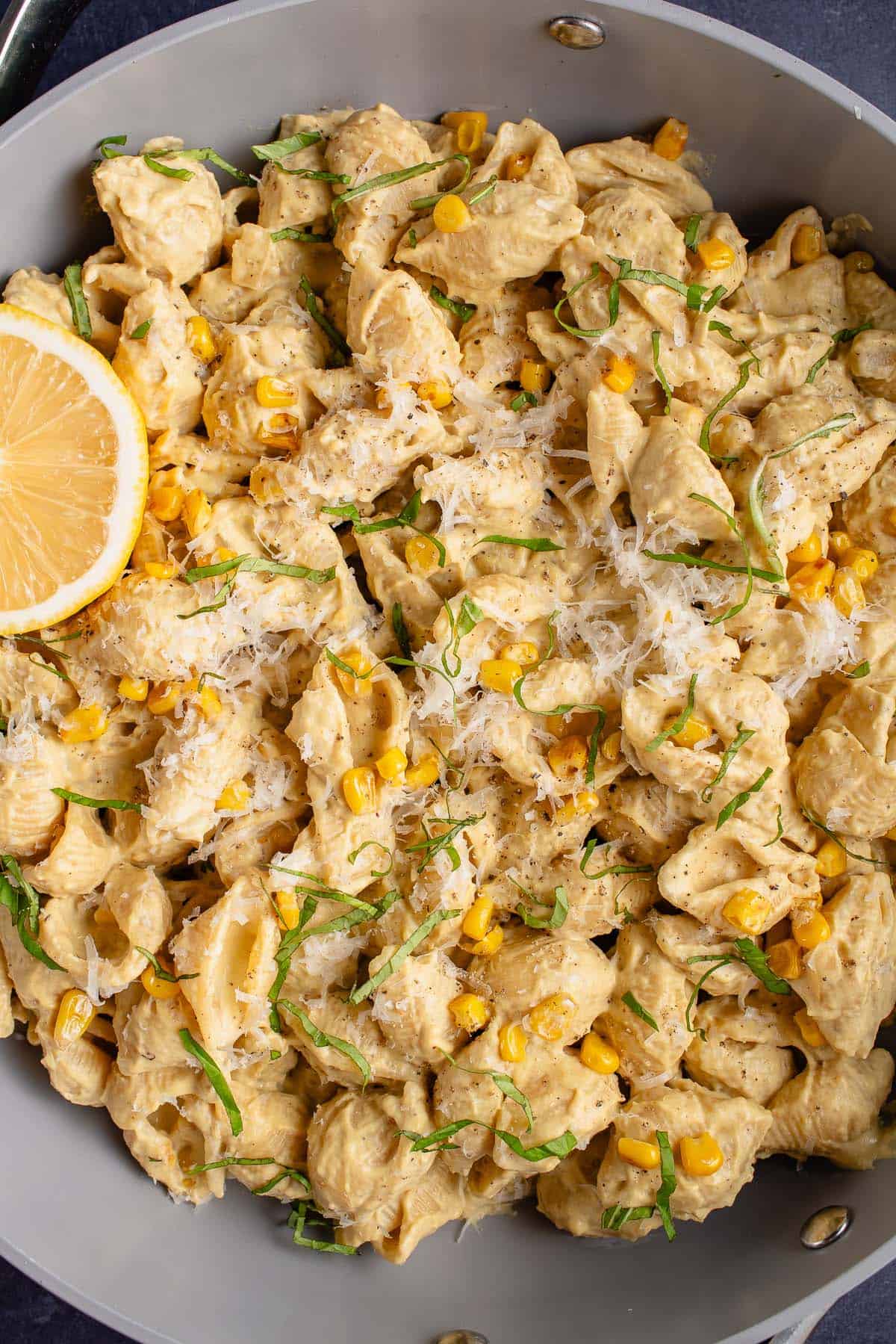 pan filled with creamy corn pasta and a lemon wedge 