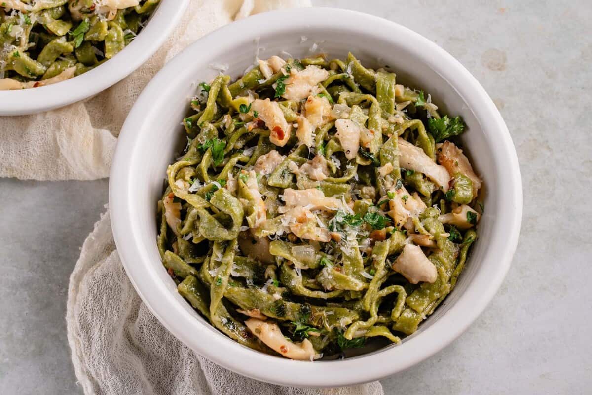 horizontal photo of fresh spinach pasta in white bowl with mushroom butter sauce