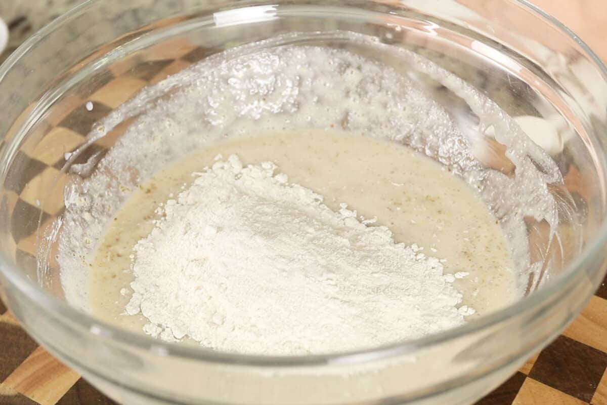 adding flour to bread dough in glass bowl