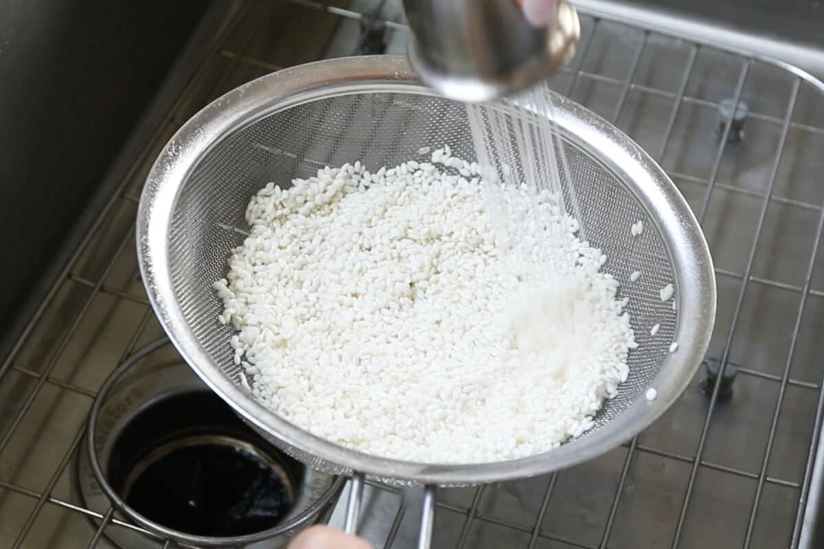 rinsing sweet rice in strainer in sink
