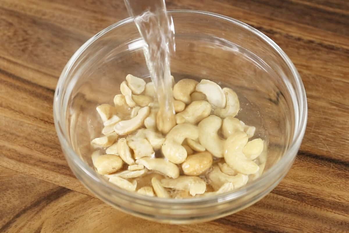 pouring hot water over cashews in glass bowl