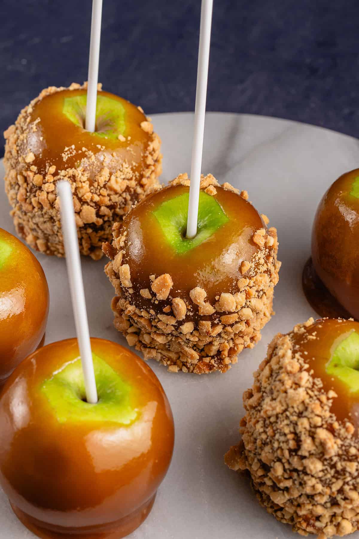 5 caramel apples with peanuts on round marble board