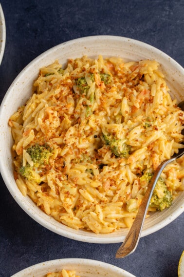 broccoli cheddar orzo with breadcrumbs in beige bowl with spoon