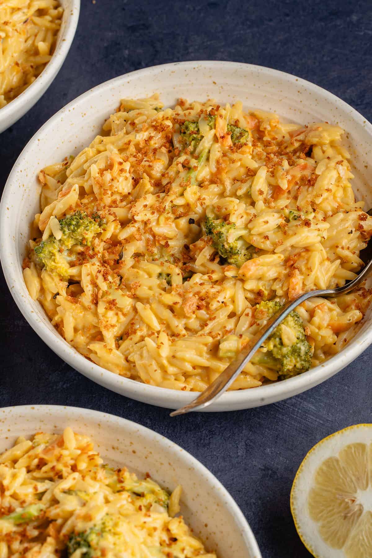 broccoli cheddar orzo with breadcrumbs in beige bowl with metal spoon