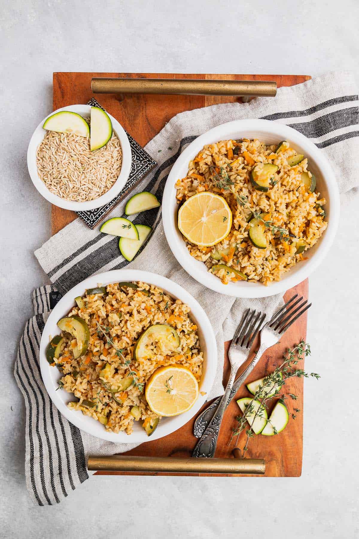 try with two bowls of rice pilaf, forks, and a napkin, small bowl of rice and zucchini slices on a grey background