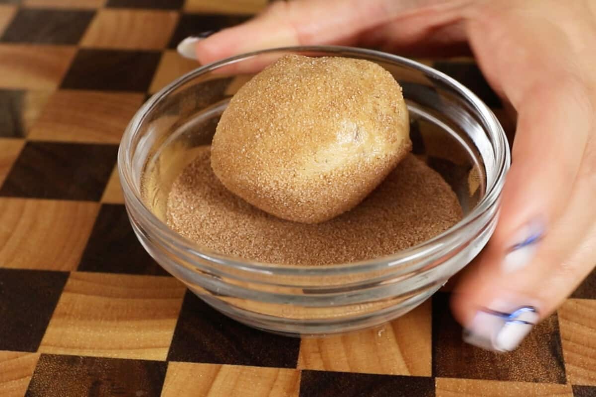 ball of dough being rolled in cinnamon and sugar