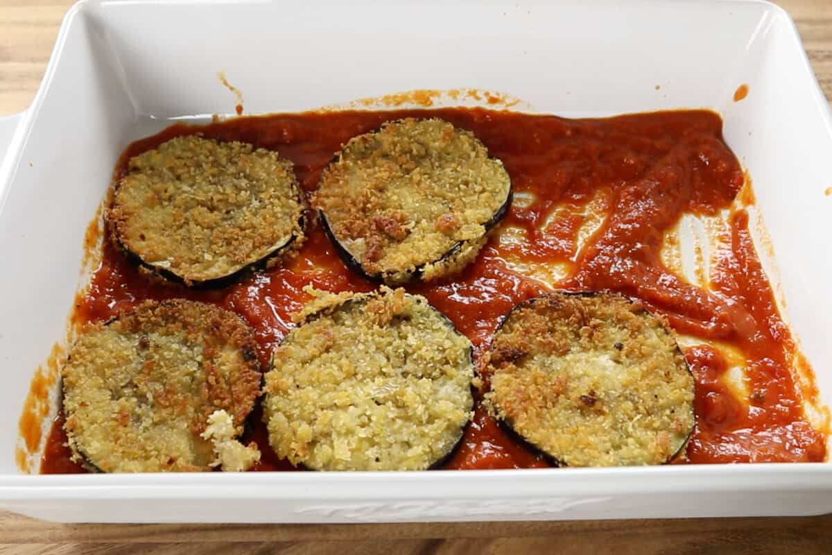 step by step - adding fried eggplant slices into baking dish with marinara sauce