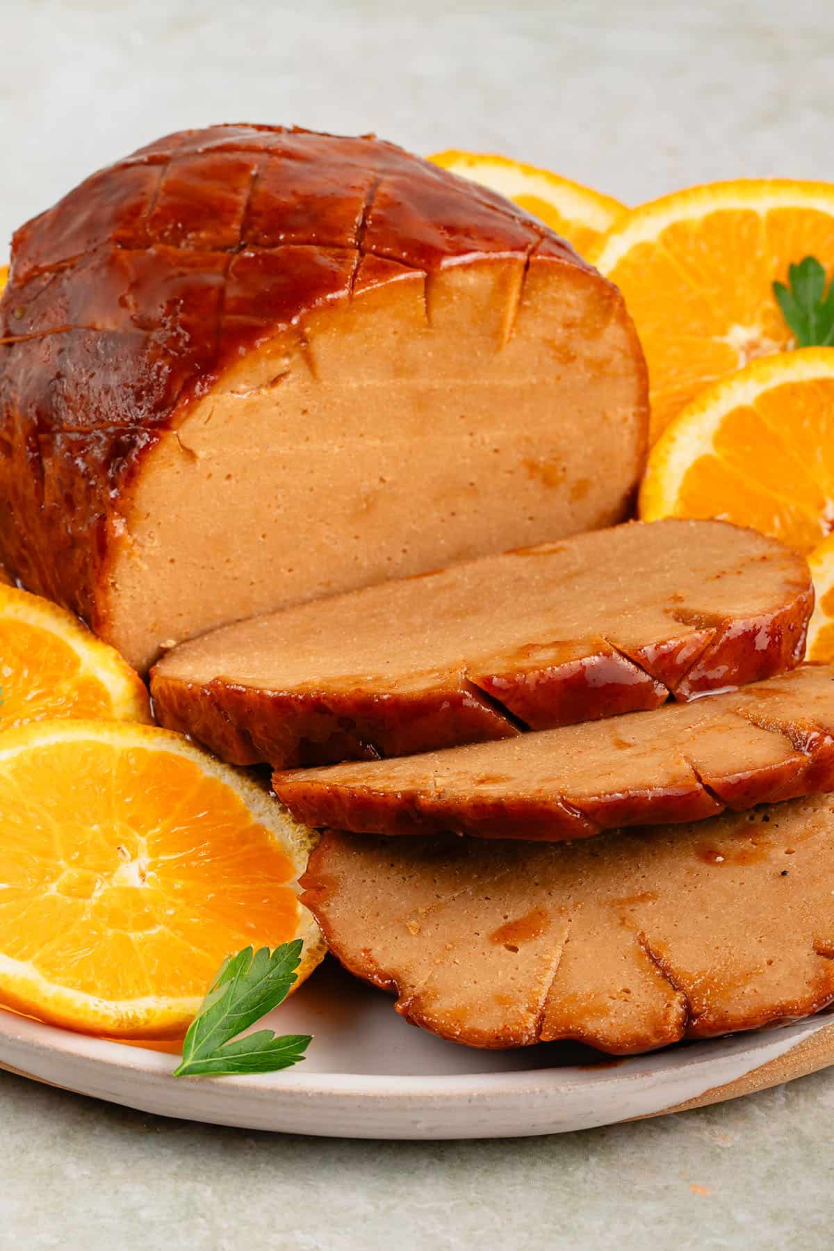 sliced vegan ham roast on plate with oranges