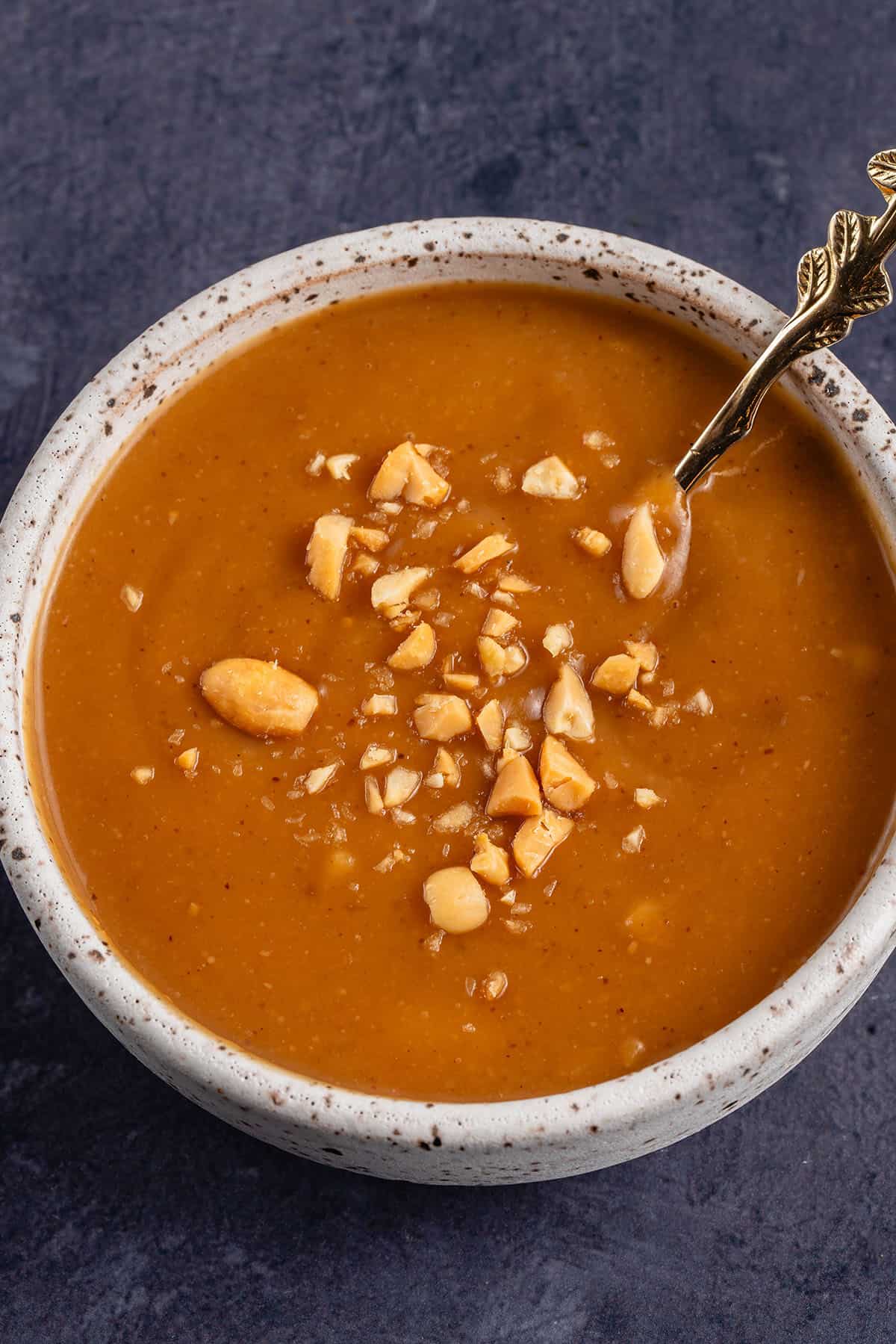 bowl of peanut sauce with peanuts on top and spoon inside