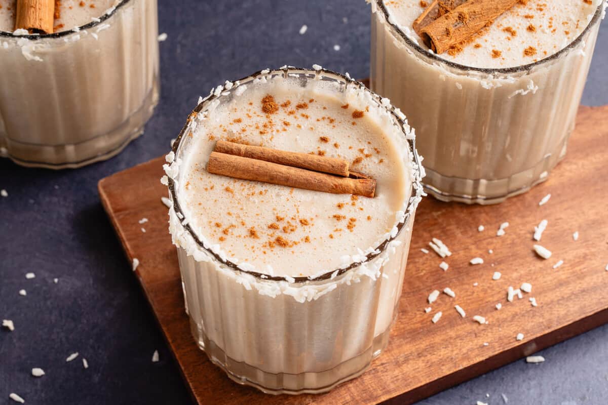 horizontal photo of 3 cups of coquito with cinnamon sticks
