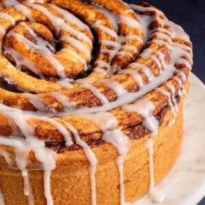giant cinnamon roll cake on a stand with icing dripping off the side