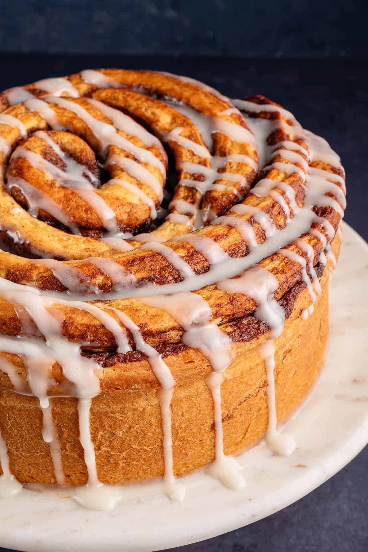giant cinnamon roll cake on a stand with icing dripping off the side