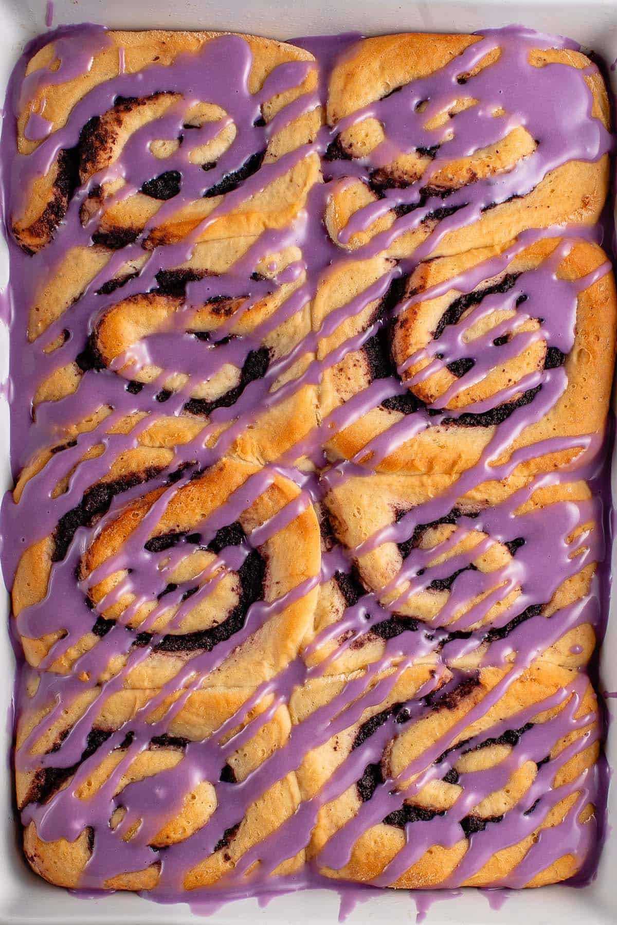 baked ube cinnamon rolls with purple icing in white dish 