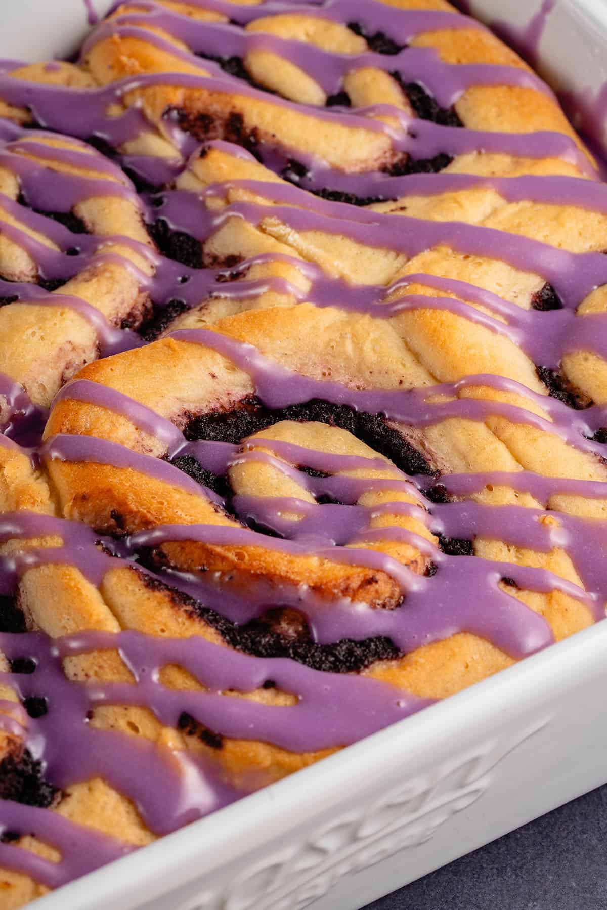 close up of baked ube cinnamon rolls with purple icing in white dish