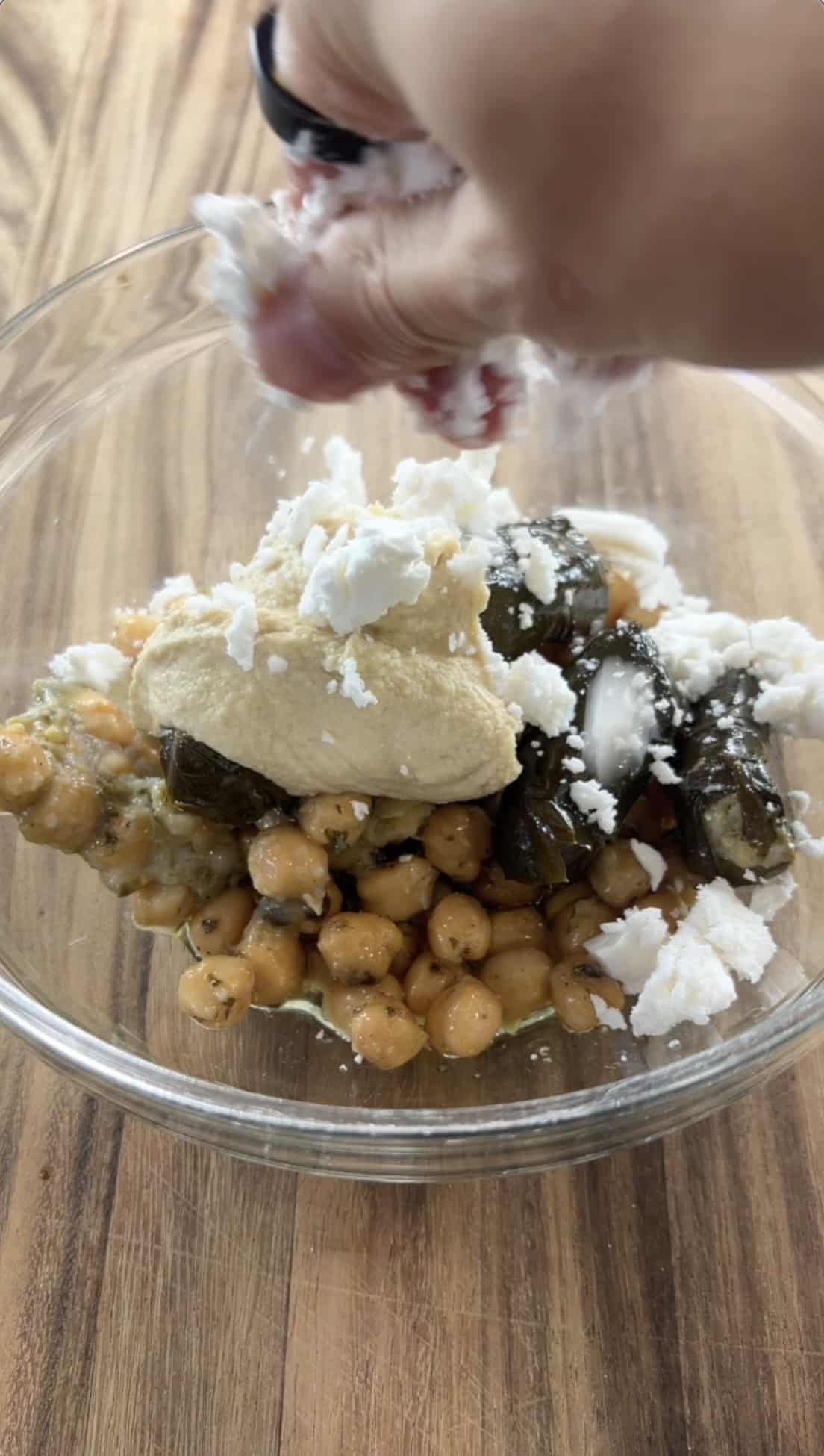 crumbling dairy-free feta into the bowl of hummus, chickpeas, and dolmas