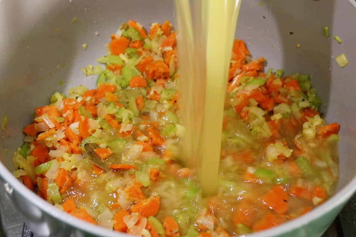 adding broth to Vegan Lemon Chicken Orzo Soup in large pot