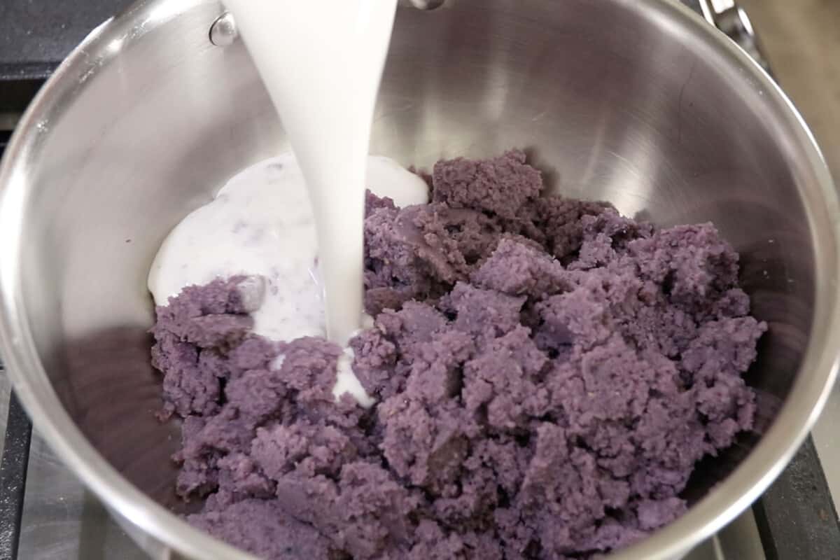 adding ube and coconut milk to stainless steel pot for ube halaya recipe