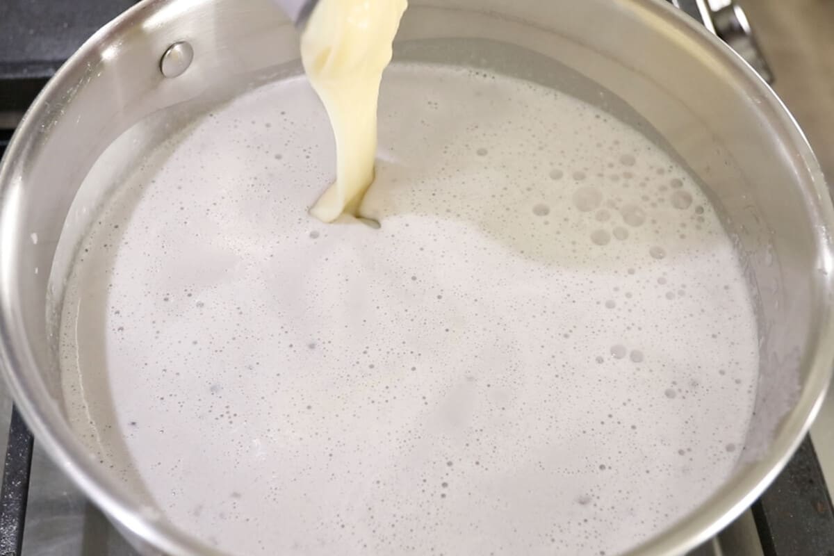 adding condensed milk to stainless steel pot for vegan ube halaya recipe