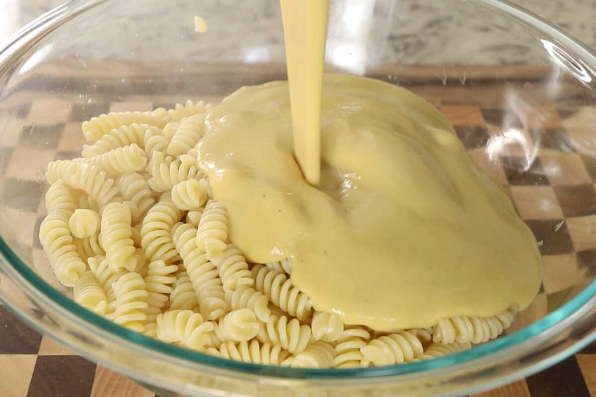 pouring Creamy White Bean sauce over Pasta in glass bowl