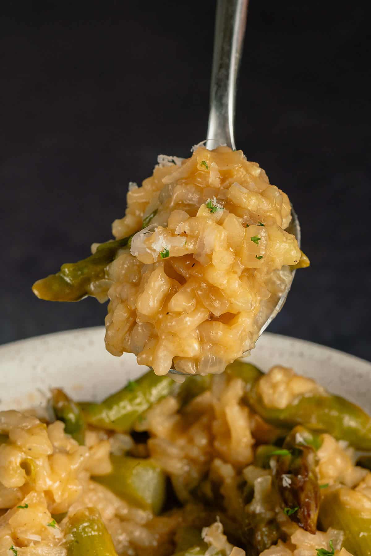 spoonful of creamy risotto with asparagus on a black background