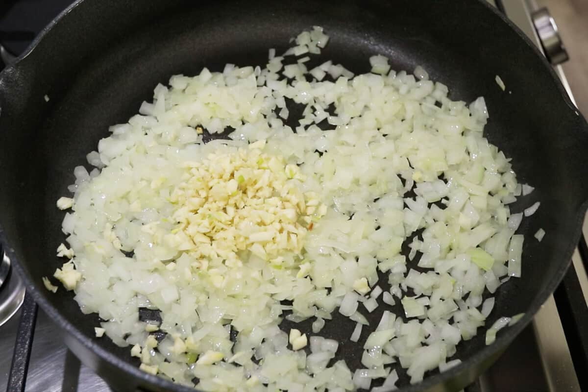 garlic being added to sautéed onions in a pan