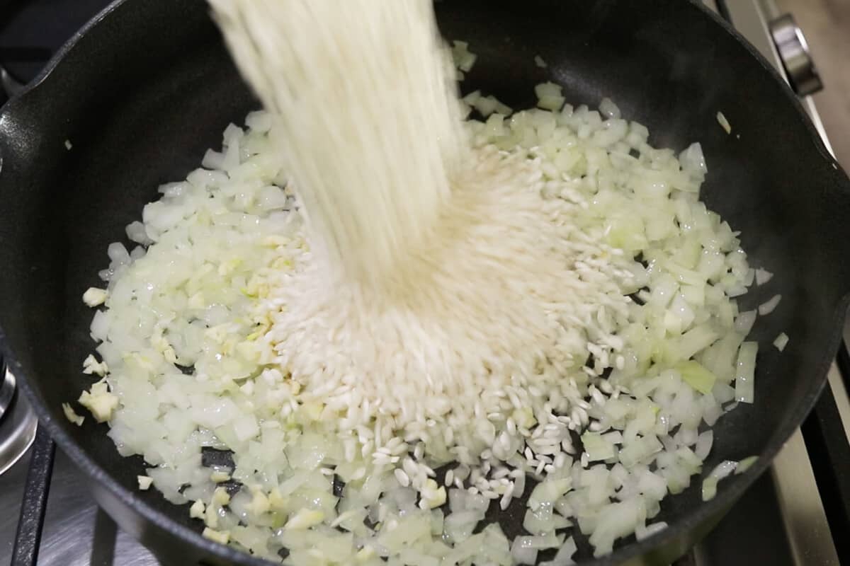 rice being poured over cooked onions in a pan