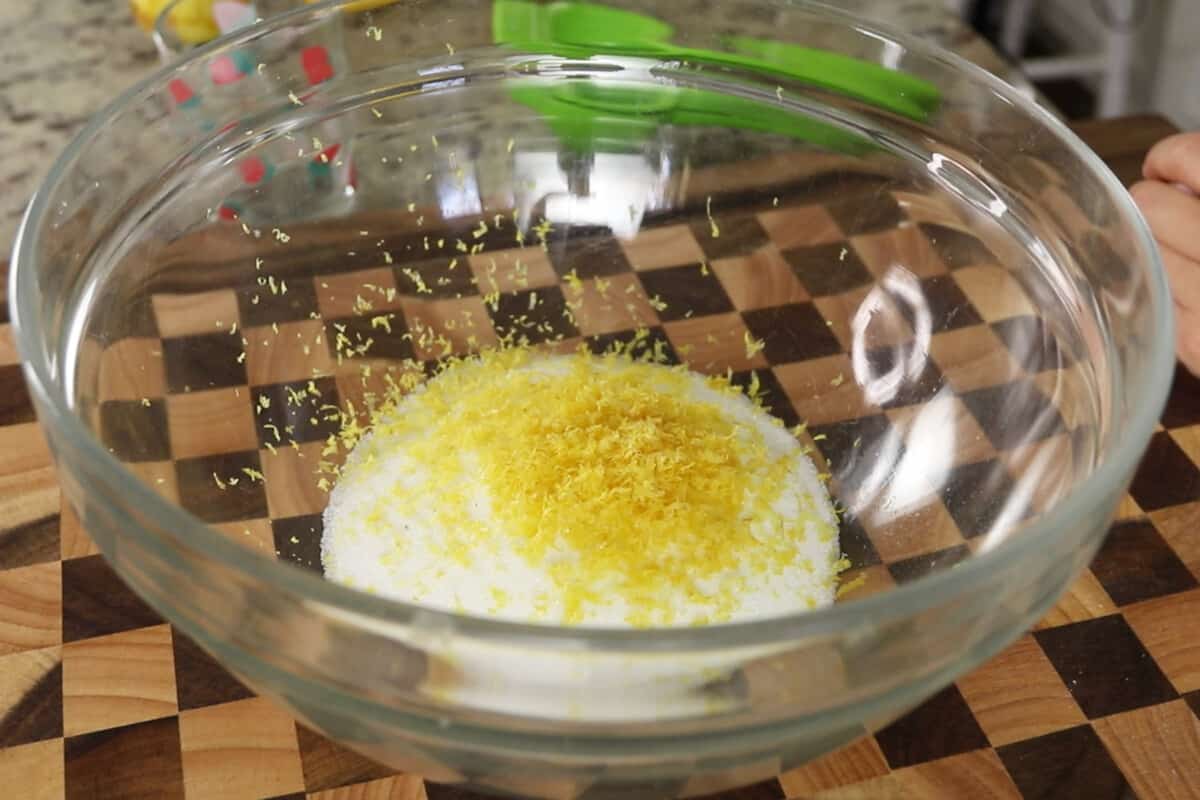 mixing fresh lemon zest with sugar in glass bowl for lemon loaf